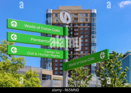 Green, World of Coca Cola signpost à Atlanta en face de problèmes de mise au point et gratte-ciel ciel bleu et arbres en arrière-plan Banque D'Images