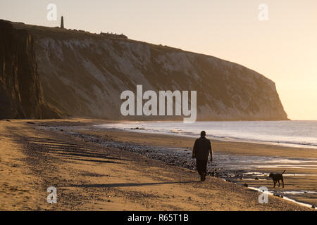 Un homme promenait son chien pendant le lever du soleil à Yaverland Beach sur l'île de Wight, Royaume-Uni Banque D'Images