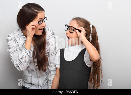 Heureux surprenant la mère et l'exciter à la mode pour enfants lunettes à chaque autre avec bouche ouverte sur l'espace copie vide arrière-plan. Banque D'Images