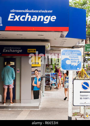 Un touriste se retire d'un distributeur de billets à côté d'un échange à l'étranger en Kata, Phuket, Thaïlande ; avec un signe de la zone de danger de tsunami dans l'avant-plan. Banque D'Images