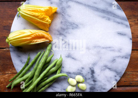 Les fleurs de courgettes jaunes, haricots verts et les fèves, sur fond blanc et bleu en planche, les légumes sont disposés sur le côté gauche de t Banque D'Images