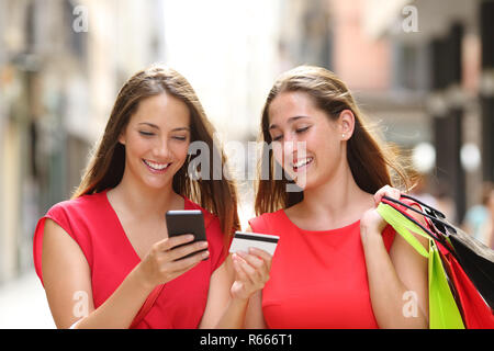 Vue de face de deux professionnels shoppers acheter en ligne avec carte de crédit et téléphone portable marche dans la rue Banque D'Images