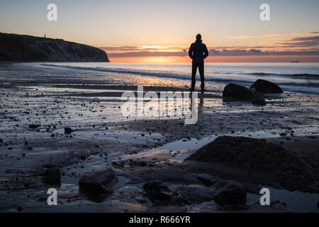 Un homme observe le lever du soleil sur la baie de Sandown, sur l'île de Wight Banque D'Images