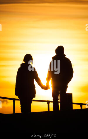 Un couple (homme et femme) à l'âge de 20 ans, il y a début des années 30 tant qu'ils marchent main dans la main pendant le coucher du soleil le long de la promenade à Southsea, UK Banque D'Images
