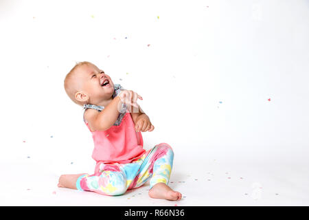 Laughing toddler girl est à la recherche jusqu'à la chute de confettis papier sur son Banque D'Images