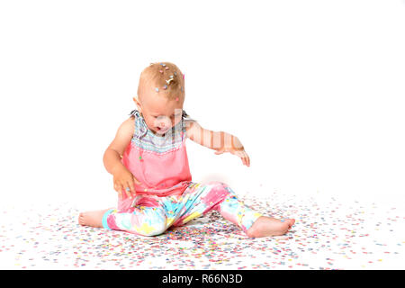 Laughing toddler girl est à la recherche à l'étage sur papier tombé confetti Banque D'Images