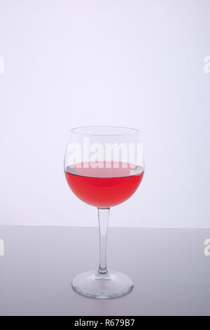 Un verre avec une boisson rouge sur une surface blanche Banque D'Images