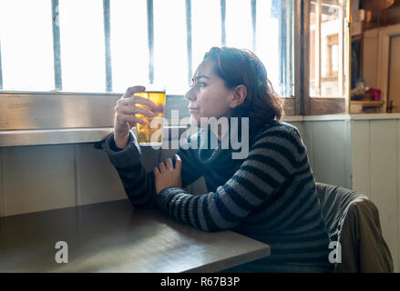 Portrait d'une jolie femme latine de boire une bière dans un pub bar déprimé triste et solitaire dans la dépression et l'abus d'alcool santé mentale Banque D'Images