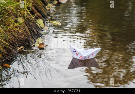 Papier blanc solitaire appelé bateau flottant sur un ruisseau de paix outdoor le sombre jour d'automne closeup Banque D'Images