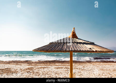 Gros plan avec une faible profondeur de champ d'un parapluie de plage tropicale fait de paille en face d'une mer turquoise de flou artistique. Banque D'Images