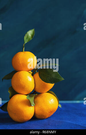 Haute pile des mandarins avec feuilles jaune est allongé sur fond bleu. Banque D'Images