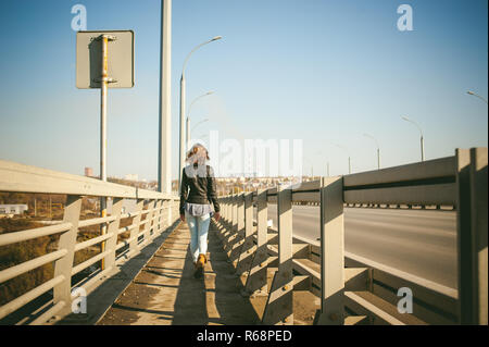 Fille va sur road bridge. lonely woman veste en cuir noire de l'automne, marcher sur le pont qui va transporter. Banque D'Images