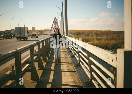 Fille va sur road bridge. lonely woman veste en cuir noire de l'automne, marcher sur le pont qui va transporter. Banque D'Images