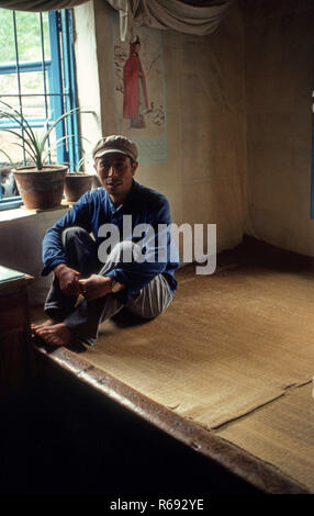 Le nord de la Chine 1980 située dans Waoning Province dans un intérieur d'une maison où un homme est assis sur un lit kang une cuisinière qui est une plate-forme de brique où l'air canalisé est alimentée par un incendie offrant chaleur, généralement en bois de feu. Banque D'Images