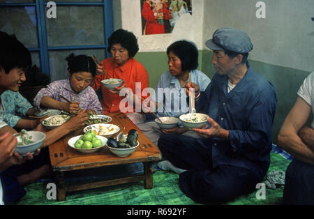 Le nord de la Chine 1980 située dans Waoning Province dans un intérieur d'une maison où une famille mangent un repas assis sur un lit kang une cuisinière qui est une plate-forme de brique où l'air canalisé est alimentée par un incendie offrant chaleur, généralement en bois de feu. Banque D'Images