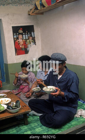 Le nord de la Chine 1980 située dans Waoning Province dans un intérieur d'une maison où une famille mangent un repas assis sur un lit kang une cuisinière qui est une plate-forme de brique où l'air canalisé est alimentée par un incendie offrant chaleur, généralement en bois de feu. Banque D'Images