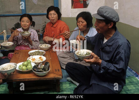 Le nord de la Chine 1980 située dans Waoning Province dans un intérieur d'une maison où une famille mangent un repas assis sur un lit kang une cuisinière qui est une plate-forme de brique où l'air canalisé est alimentée par un incendie offrant chaleur, généralement en bois de feu. Banque D'Images