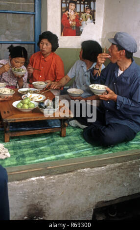 Le nord de la Chine 1980 située dans Waoning Province dans un intérieur d'une maison où une famille mangent un repas assis sur un lit kang une cuisinière qui est une plate-forme de brique où l'air canalisé est alimentée par un incendie offrant chaleur, généralement en bois de feu. Banque D'Images