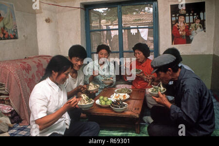 Le nord de la Chine 1980 située dans Waoning Province dans un intérieur d'une maison où une famille mangent un repas assis sur un lit kang une cuisinière qui est une plate-forme de brique où l'air canalisé est alimentée par un incendie offrant chaleur, généralement en bois de feu. Banque D'Images