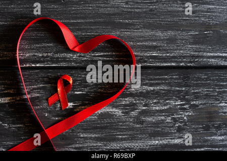 Libre de ruban rouge en forme de cœur sur la table en bois noir pour l'arrière-plan de la campagne de la journée mondiale du sida. Banque D'Images