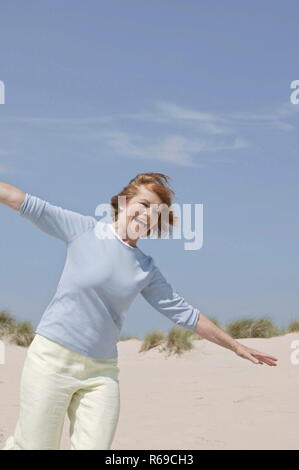 Strandszene, Portrait, Frau, Mitte 50, mit kurzem Freizeitkleidung laeuft roetlichen Haar dans ausgebreiteten Duenen mit Armen die herunter Banque D'Images