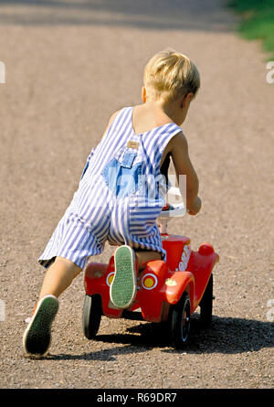 Portrait, Outdoor, blonder Junge spielt mit einem roten Bobbycar im Park Banque D'Images