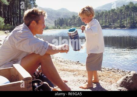 Piscine, Ganzfigur 6 Jahre alter, blonder Junge schenkt Am Ufer voit von seinem im Wald von Vateraus blauen Kanne etwas zu trinken eine dans Blechtasse ein Banque D'Images