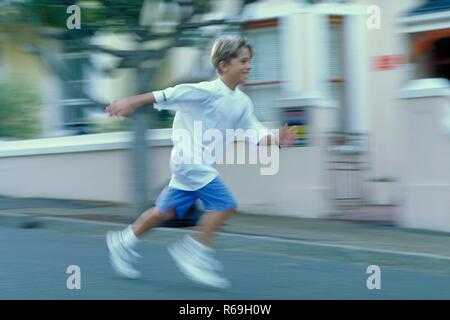 Portrait, Ganzfigur, 8 Jahre alter blonder Junge bekleidet mit weissem T-Shirt blauen und einem une laeuft Short Haus vorbei die Strasse entlang Banque D'Images