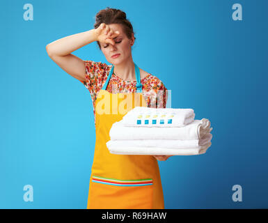 Assez jeune femme en tablier orange avec linge blanc isolé sur bleu. La chambre est propre, le linge est lavé - Disque à domicile n'est plus Banque D'Images