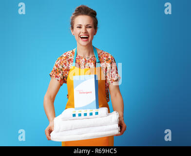 Portrait de jeune femme en tablier orange de nappes blanches et de détergent en poudre sur fond bleu. Comment choisir la lessive ? Efficace, env Banque D'Images