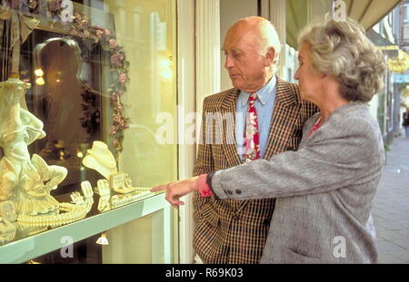 Seniorenpaar, gepflegter Herr mit Anzug unt roter Krawatte schaut mit Gattin senneur bekleidet Kostuem die grauen im von Antiquitaetengeschaeftes Auslagen un Banque D'Images