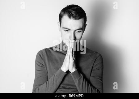 Close up portrait noir et blanc d'un jeune homme portant un cavalier col roulé, mains ensemble, contre un arrière-plan studio Banque D'Images