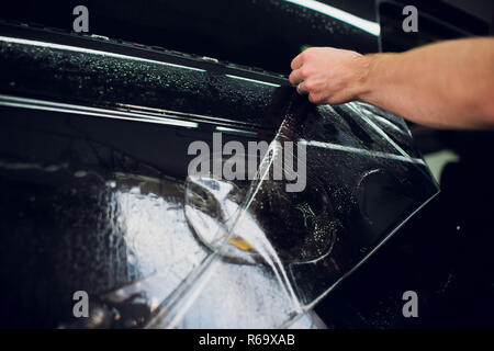 Les mains des travailleurs installe le film protecteur de peinture voiture d'enrubannage. Banque D'Images