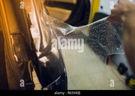 Les mains des travailleurs installe le film protecteur de peinture voiture d'enrubannage. Banque D'Images