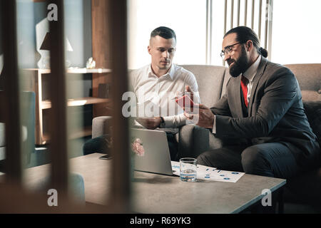 Patron barbu et son jeune stagiaire assis sur le canapé tout en parlant Banque D'Images