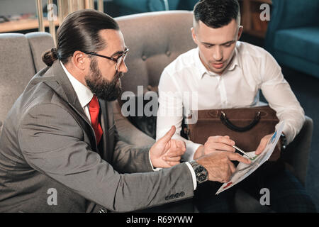 Patron barbu à ses moments de travail expliquant jeune stagiaire Banque D'Images