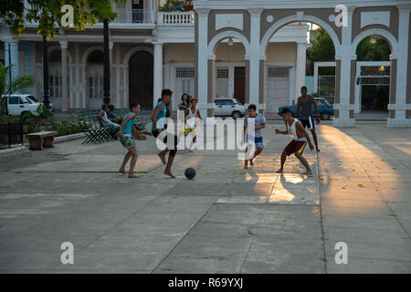 Cuban boys jouant au football sur la place principale de Cienfuegos Cuba comme le soleil commence à définir d'une lueur dorée sur la rue Banque D'Images