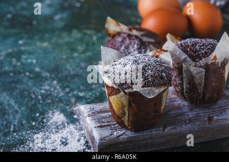 Muffin carottes-chocolat saupoudrés de sucre glace, une tasse de thé, ingrédients. La farine, les oeufs, le citron les agrumes sur un tableau sombre de l'espace de copie Banque D'Images