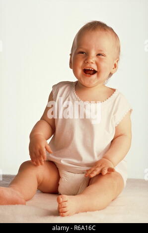 Portrait, bébé, 10 Monate, mit weissem bekleidet Hemdchen und Windeln, sitzt vor Freude auf einem Schaffell lachend Banque D'Images