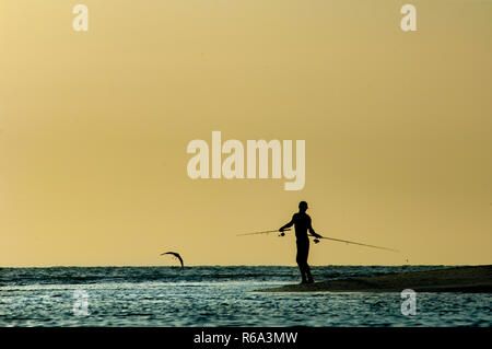 Une silhouette d'homme poissons au coucher du soleil le long de Barefoot Beach, en Floride. Banque D'Images