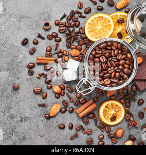 Café dans un bocal en verre avec des haricots, du chocolat, des oranges séchées, des bâtons de cannelle et anis sur fond de béton gris. Concept de café avec spi différents Banque D'Images