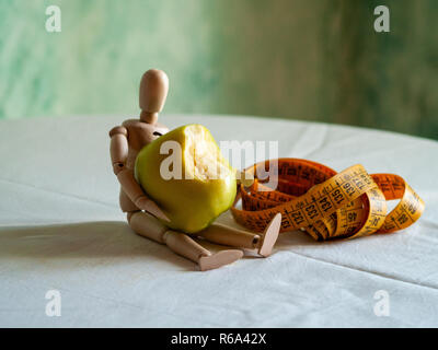 Une figurine en bois avec un mordu de pomme verte et d'un ruban de mesure, sur une table Banque D'Images