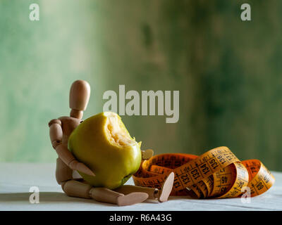 Une figurine en bois avec un mordu de pomme verte et d'un ruban de mesure, sur une table Banque D'Images