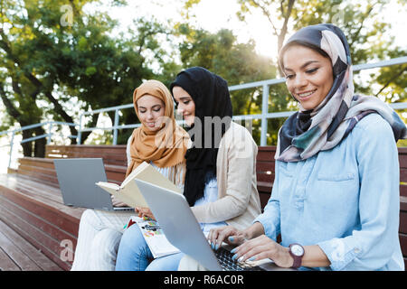 Photo de femmes portant des headscarfs islamique joyeux se reposant dans Green Park et de l'étude sur l'ordinateur portable Banque D'Images