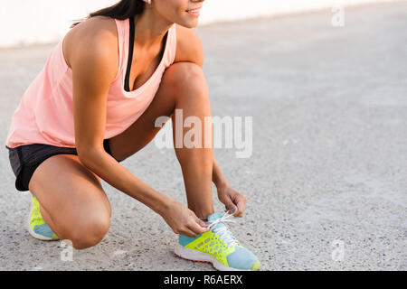 Photo recadrée de belle femme 20s en s'accroupissant et en attachant son survêtement lacets sneaker sur demande lors de l'entraînement à seaside Banque D'Images