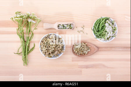 Vue de dessus de fruits frais et secs des fleurs et des feuilles d'achillée avec cuillères et bol avec un fond de bois Banque D'Images