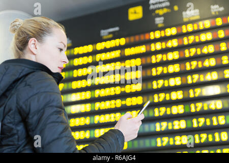 Femme à l'aéroport en face du conseil d'information de vol de contrôle de son téléphone. Banque D'Images