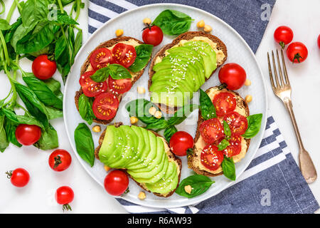 L'avocat et les tomates sandwiches sains d'hummus, sésame et basilic dans une plaque avec serviette et bifurquer au-dessus de l'arrière-plan en marbre blanc. La nourriture végane. haut de la vie Banque D'Images