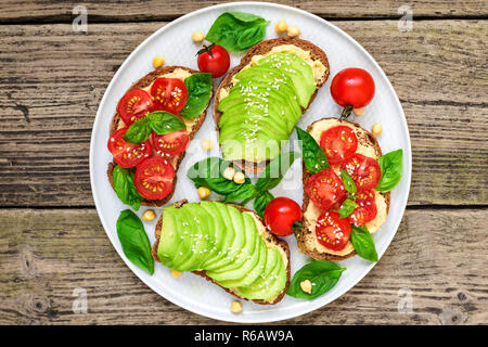 L'avocat et les tomates sandwiches sains d'hummus, sésame et basilic dans une plaque sur fond de bois rustique. La nourriture végane. Vue de dessus Banque D'Images