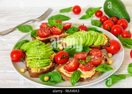 L'avocat et les tomates sandwiches sains d'hummus, sésame et basilic dans une assiette avec une fourchette sur fond de bois blanc. La nourriture végane. close up Banque D'Images